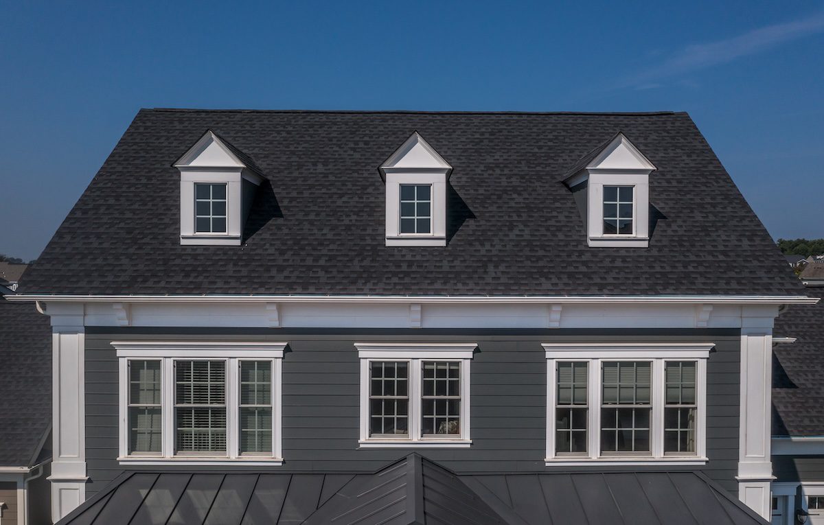 Classic symmetric front of a luxury house with two triple windows a double window, three dormer windows on the roof, white trimming  blue sky