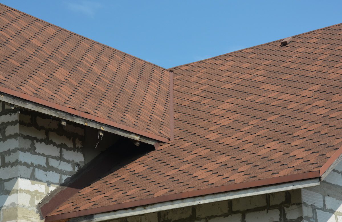 Brown asphalt shingled roof valley leaking problem area with a ventilation cap. A close-up of asphalt shingles installed on a roof valley with a waterproof flashing. Asphalt shingles roofing.