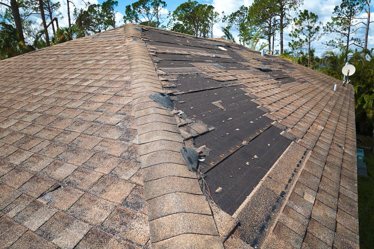 Damaged house roof with missing shingles after hurricane Ian in Florida. Consequences of natural disaster.