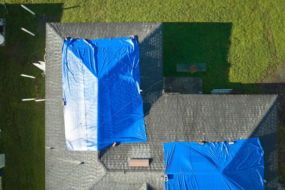 Top view of leaking house roof covered with protective tarp sheets against rain water leaks until replacement of asphalt shingles. Damage of building rooftop as aftermath of hurricane Ian in Florida.