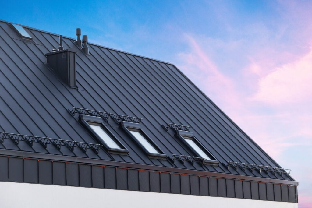 how to install metal roofing House with metal galvanized coating, chimney pipe, mansard windows and snow holding cornice on roof slope against sunset sky. Element of modern residential building with zinc rooftop sheets