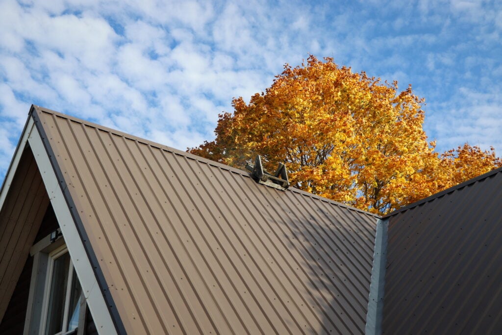how to install metal roofing Brown metalic roof house under the autmn tree against blue sky .