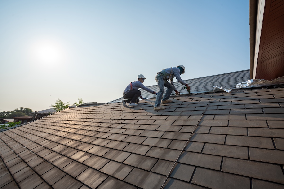 Roofer worker in special protective work wear and gloves,Using pneumatic gun and repair and replace roof tile on top of the new roof.