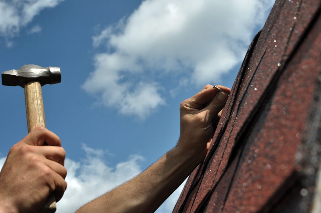 roofing tools Hand with a hammer to drive a nail, roof repairs