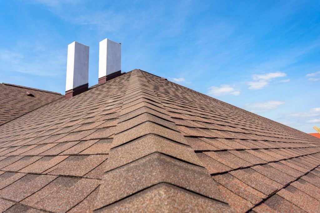 owens corning shingles Photo of new roof with asphalt tile and two white chimney on new home under construction, against blue sky