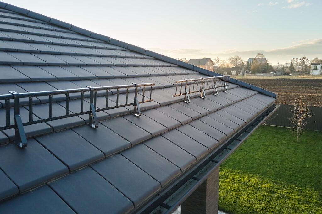 burnished slate metal roofing Closeup snow guard for safety in winter on house roof top covered with ceramic shingles. Tiled covering of building.