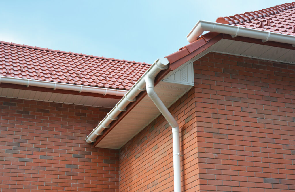 A close-up on plastic rain gutters, downspout, soffit and fascia with a box-end on the corner of a brick house as important parts of roofing system waterproofing and ventilation. roof anatomy
