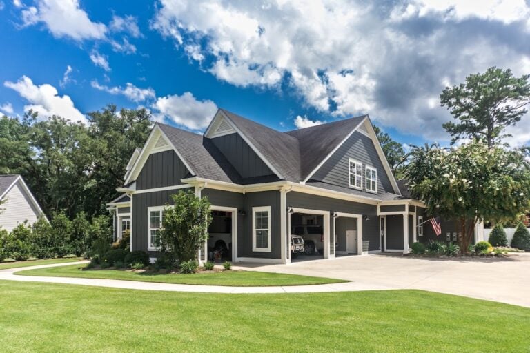 The side view of a large gray craftsman new construction house with a landscaped yard a three car garage and driveway.