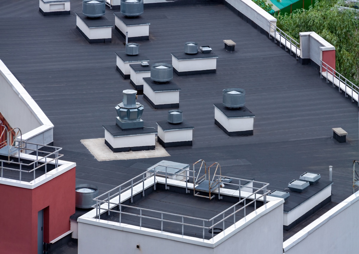 Top view flat roof with air conditioners and hydro insulation membranes on top of a modern apartment building summer day.