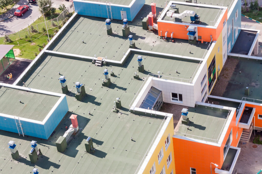 difference between multifamily and apartment Top view flat roof with air conditioners and hydro insulation membranes on top of a modern blue and orange apartment building sunny summer day.