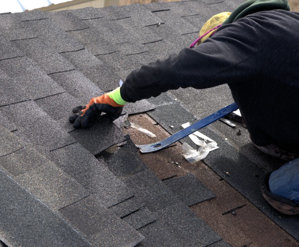 diy roof repairs Roofer uses a blue pry bar to remove damaged shinlges during the repair of a residential roof.