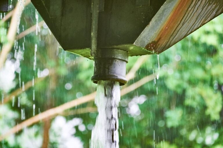 roof scupper with large amount of water running from a scupper box down a chain of metal rings due to heavy rain