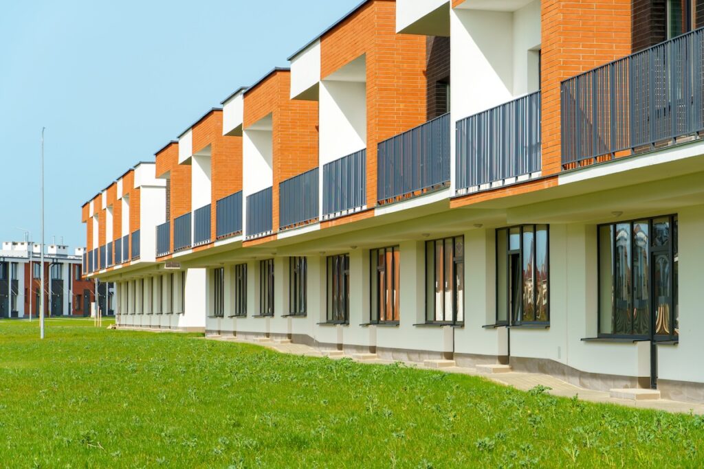 The exterior of a modern townhouse. The concept of building multi-family residential townhouses. For sale or rent a cozy small house with a beautiful green lawn.