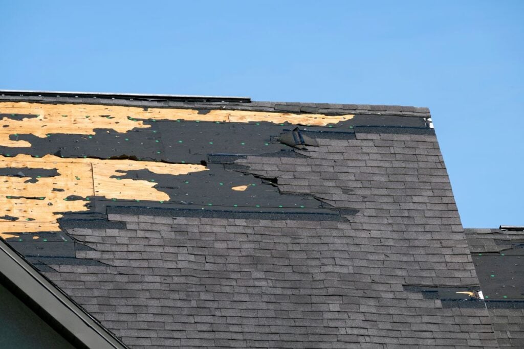 missing shingles charcoal grey roof blue sky after hurricane