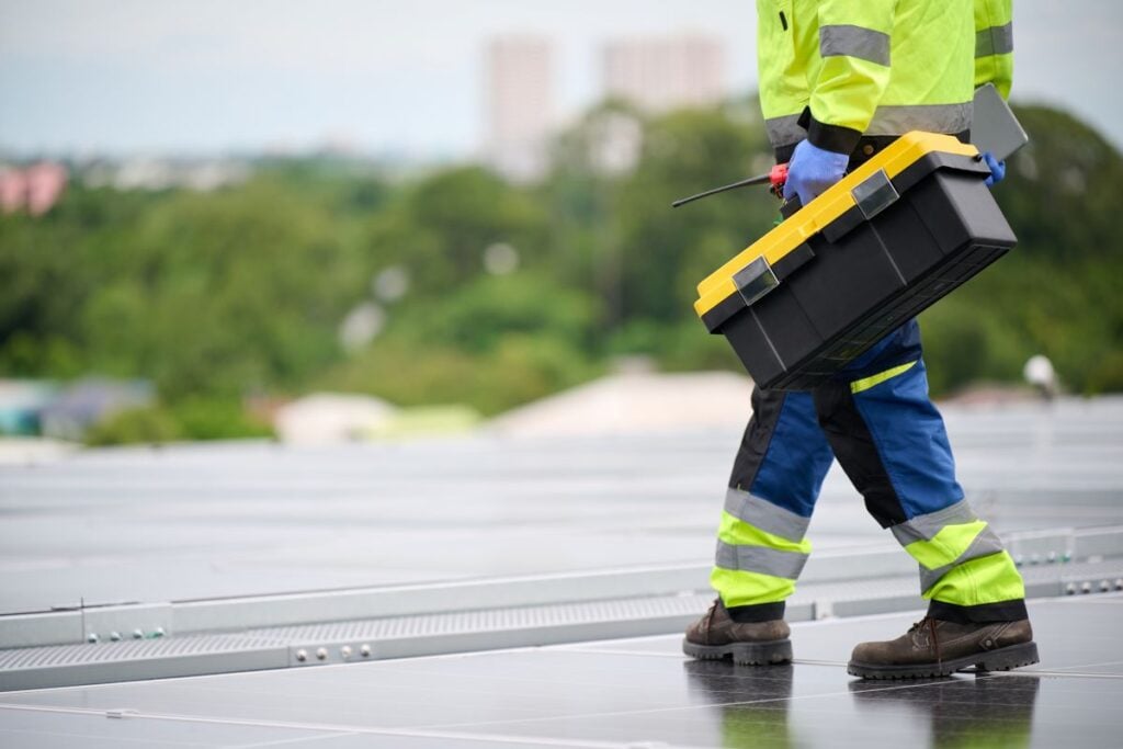 Worker holding a toolbox and inspecting the solar panel on rooftop