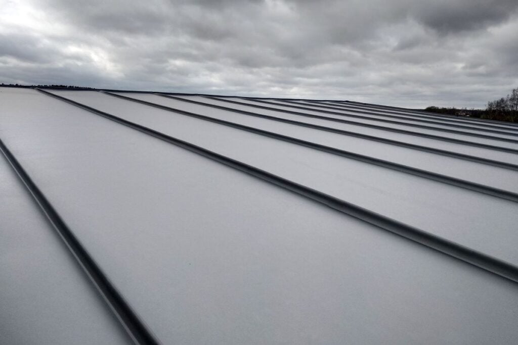 pvdf coating close-up view of a modern metal roof with PVDF coating and raised seams under a cloudy sky. The sleek roof panels create parallel lines receding into the distance, showcasing the durability and style of metal roofs in 2026.