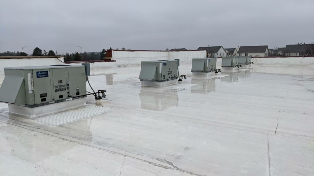 commercial roof financing Rooftop view of several large HVAC units spaced evenly across a flat, white, reflective surface on a cloudy day, with distant houses and trees visible in the background—a prime example for Commercial Roof Financing needs.