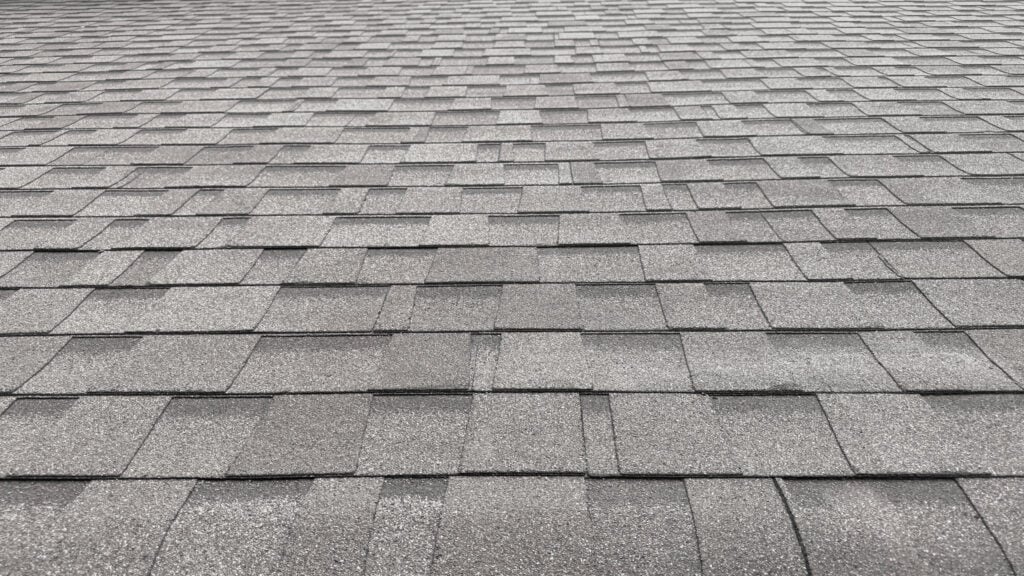 Close-up view of a gray asphalt shingle roof, showing overlapping rectangular shingles in a neat pattern. The clean, well-maintained surface is ideal for Asphalt Roof Rejuvenation, a roof replacement alternative that offers roof life extension.