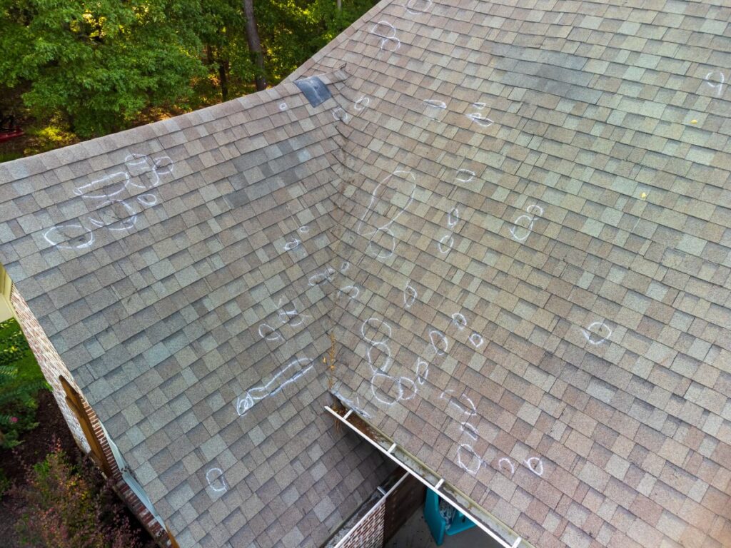 roof blistering Aerial view of a house roof with numerous chalk circles marking spots, indicating hail damage on the shingles—an issue requiring prompt roof repair. Surrounding area includes trees and part of a brick exterior wall.