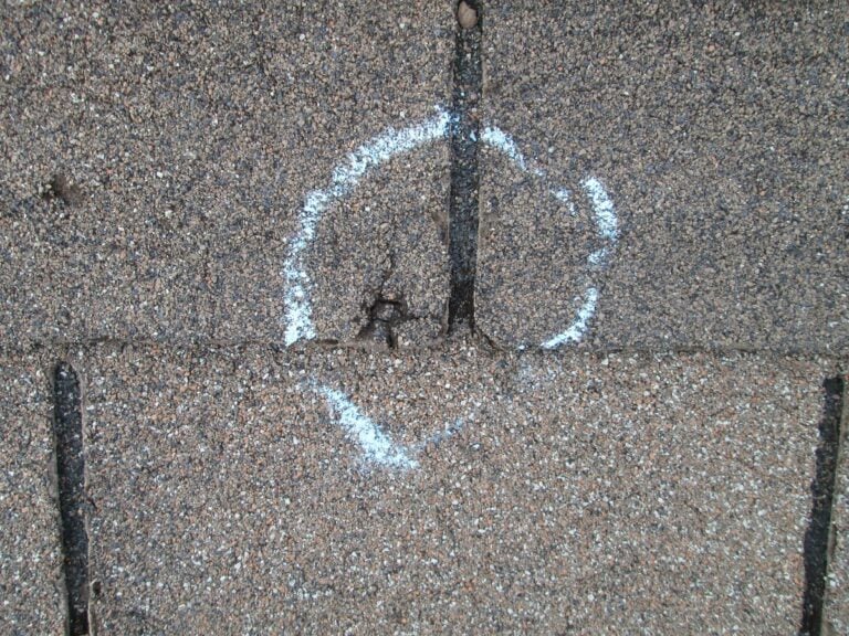 roof blistering A close-up of brown roof shingles with a white chalk circle marking a damaged or worn area where two shingles meet—a common sign of roofing problems like roof blistering.