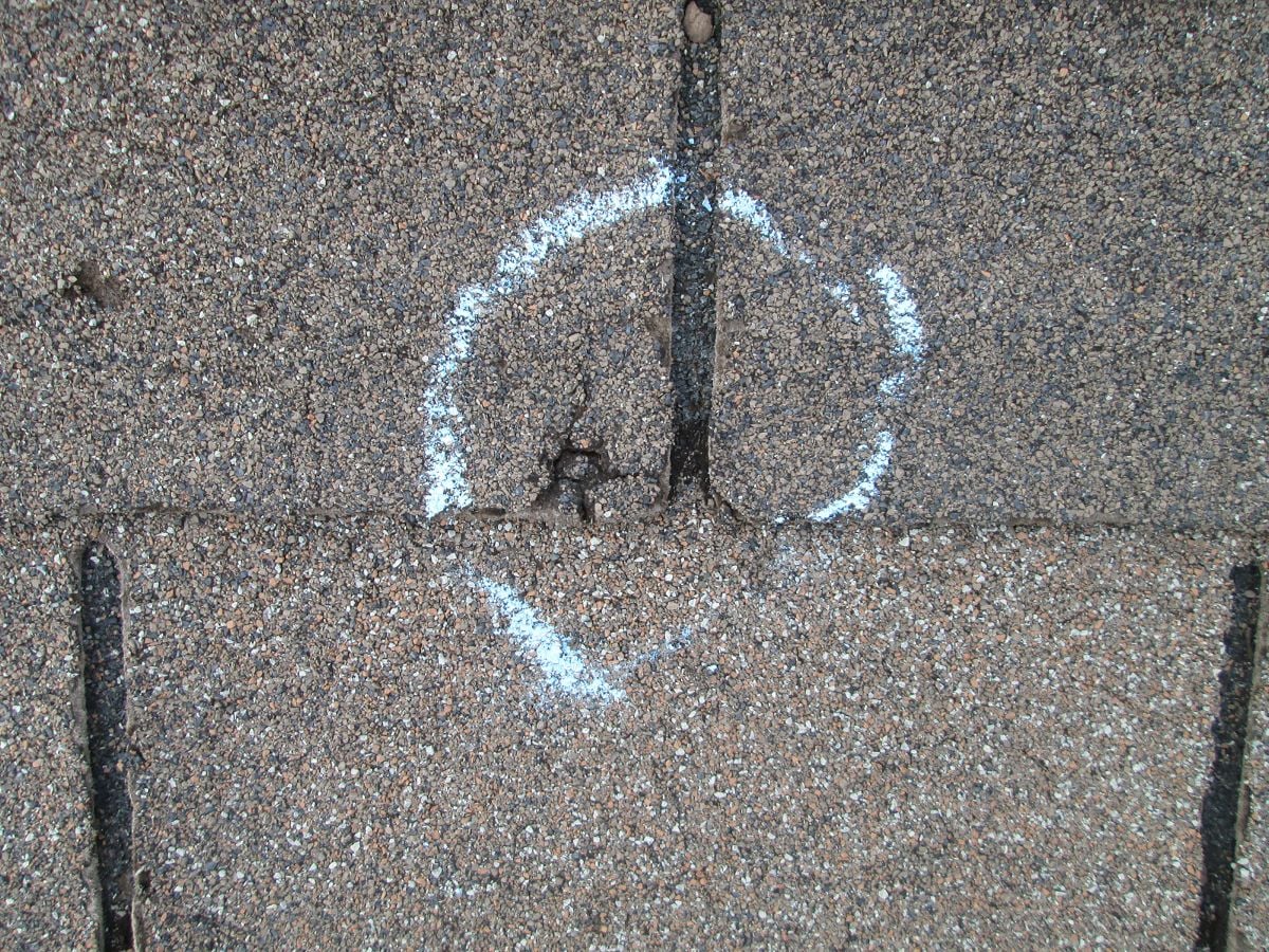 roof blistering A close-up of brown roof shingles with a white chalk circle marking a damaged or worn area where two shingles meet—a common sign of roofing problems like roof blistering.