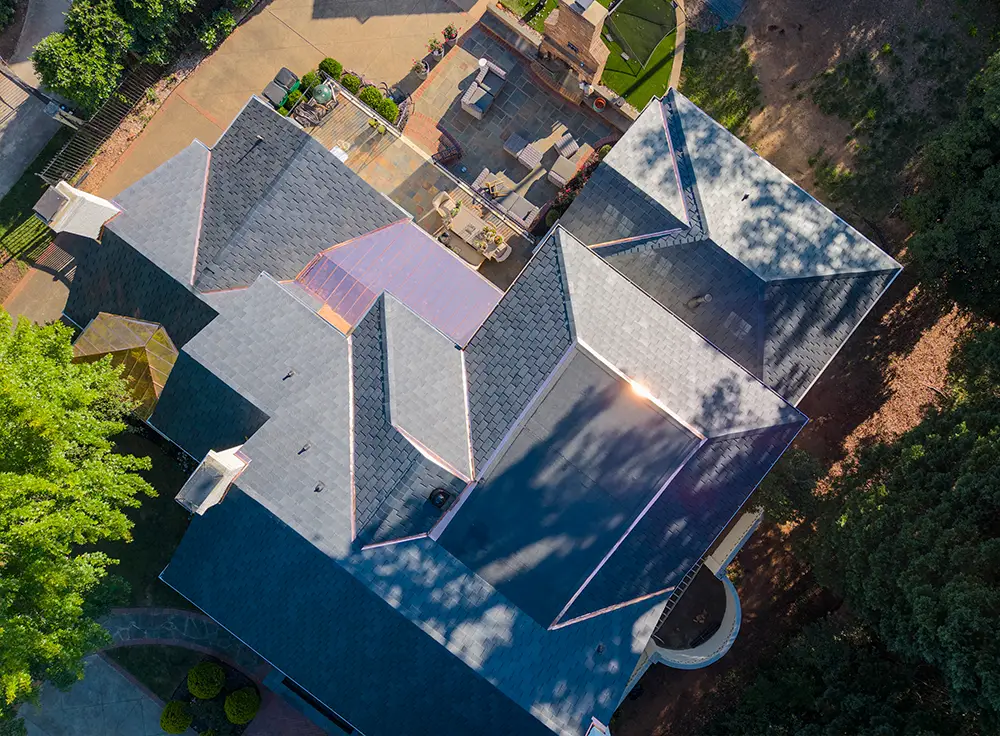 Aerial view of a large house with multiple gabled roofs and outdoor patio areas, surrounded by trees and landscaped yards—an ideal candidate for a luxury roof replacement in Greensboro, NC.