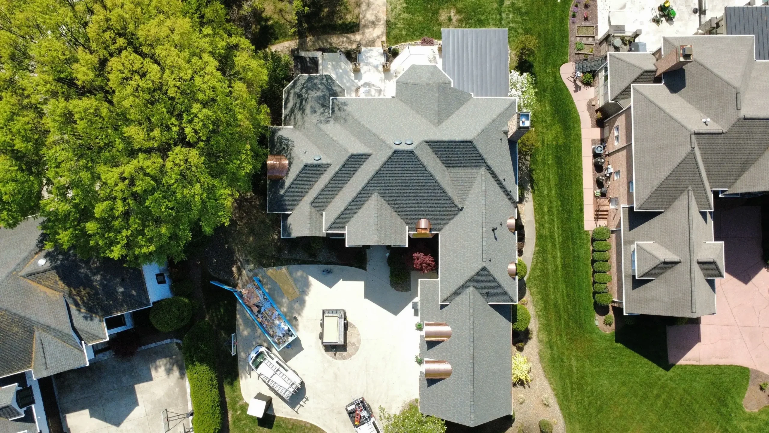 Aerial view of a large house with a gray roof, patio, scattered outdoor items, and green lawns; neighboring homes and a tree are also visible—an ideal property for anyone considering a roof replacement in Mooresville NC.