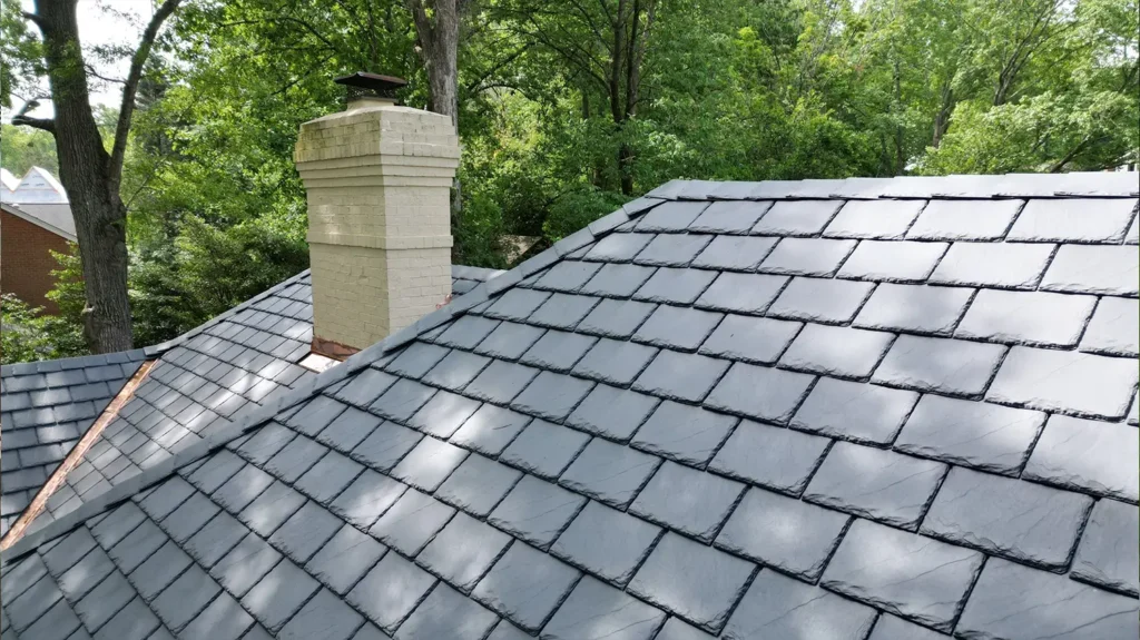 A residential roof covered in new composite slate roofing with a light-colored brick chimney.