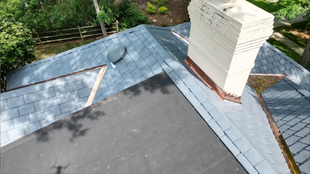Aerial view of a composite slate roof with a white brick chimney, custom copper flashing, and a flat black roof section.