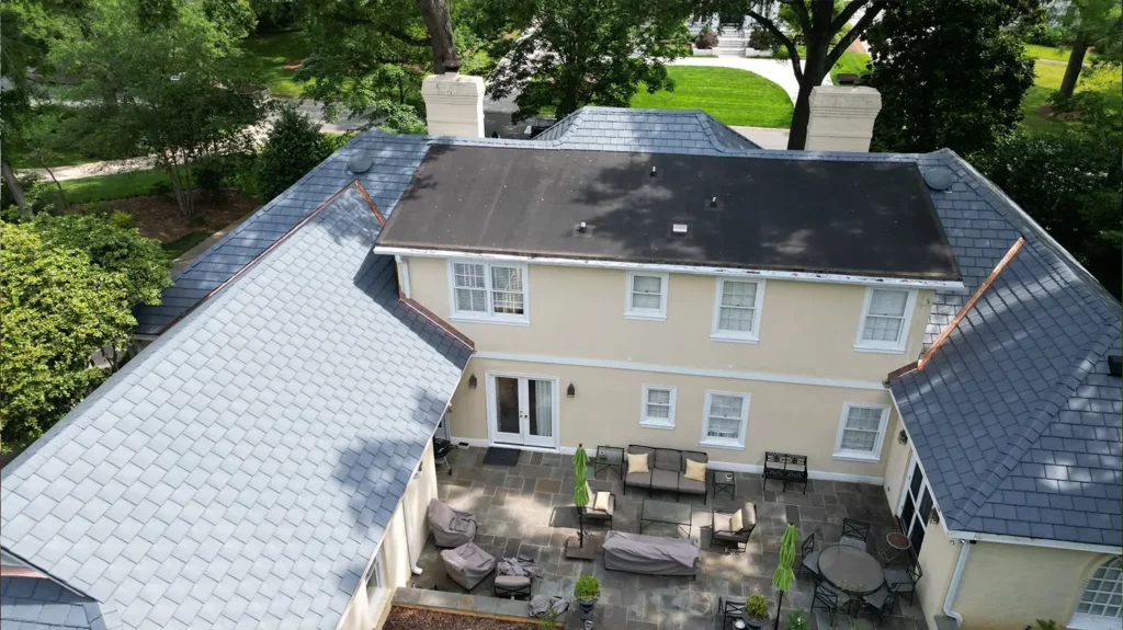 An aerial view of a tan house with a new grey composite slate roof and a paved back patio featuring outdoor furniture.