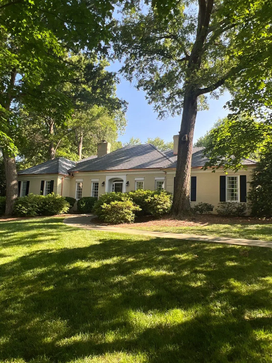 A one-story beige house with a custom copper roof, set behind a large grassy lawn and mature trees in Charlotte, NC.