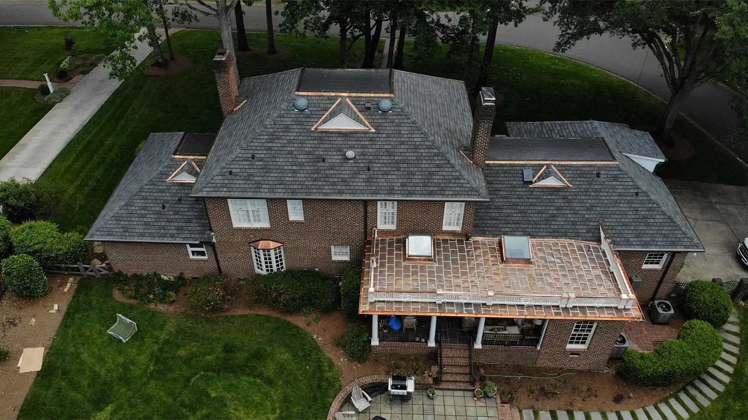 Aerial view of a two-story brick house with a new GAF Slateline roof and a flat custom copper roof over the rear patio.