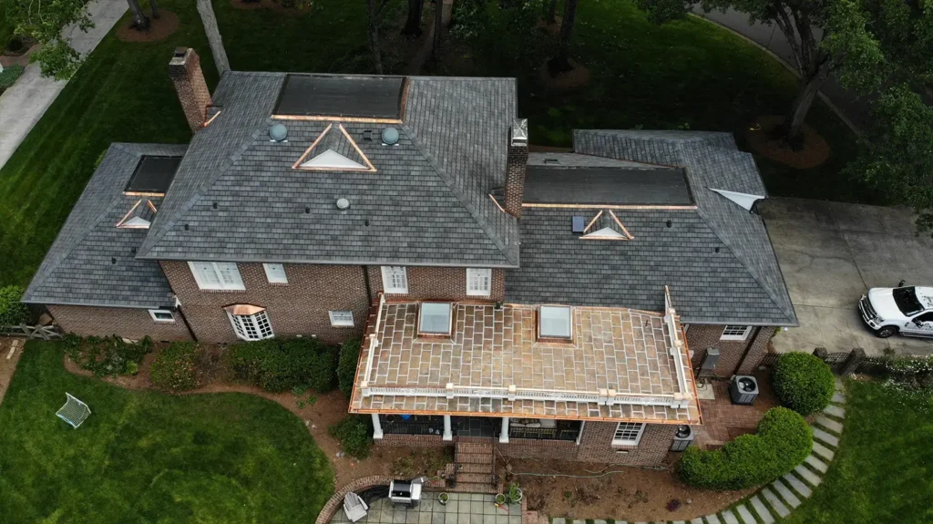 Aerial view of a brick house with a GAF Slateline roof replacement, featuring custom copper roofing, several skylights, and a flat-roofed terrace.