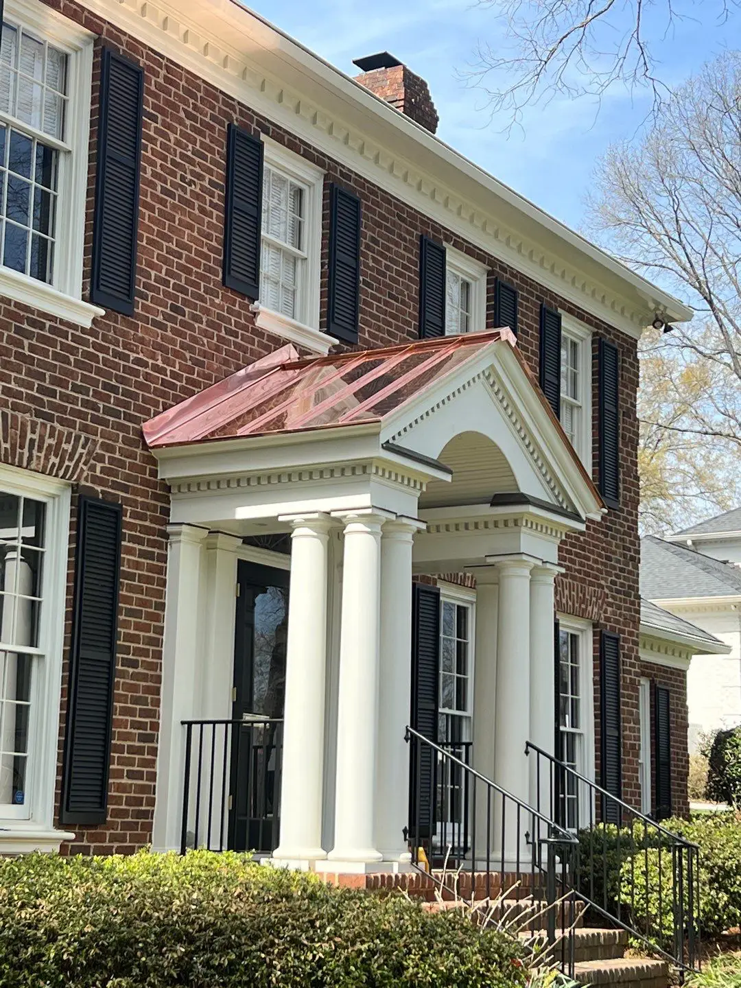 Front entrance of a brick house with a white pillared portico featuring a new custom copper roofing installation by Charlotte roofing contractors.