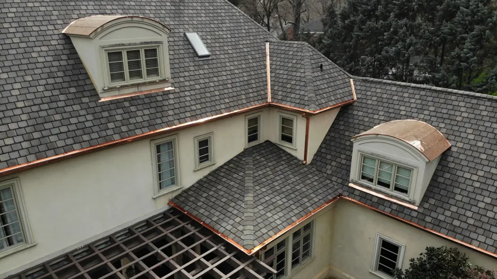 High-angle view of a house with a Highland slate roof, arched copper barrel dormers, and newly installed copper gutters and flashing.