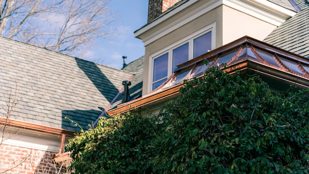 The exterior of a house with custom copper roofing and a large hedge positioned in front of a window.