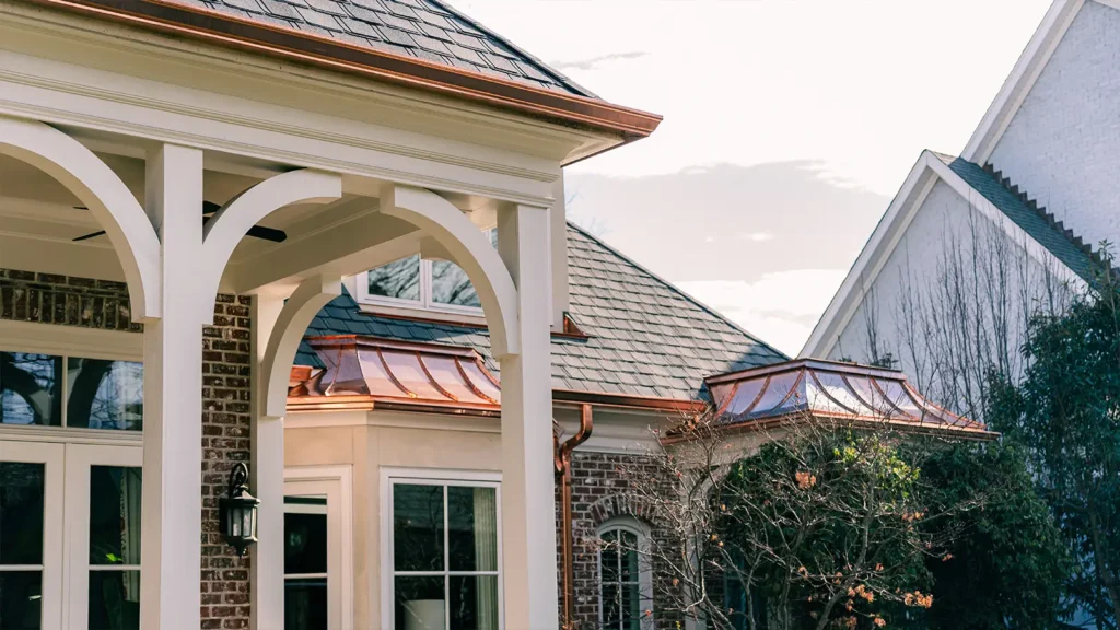Exterior view of a brick house featuring white arched porch pillars and custom copper roofing accents.