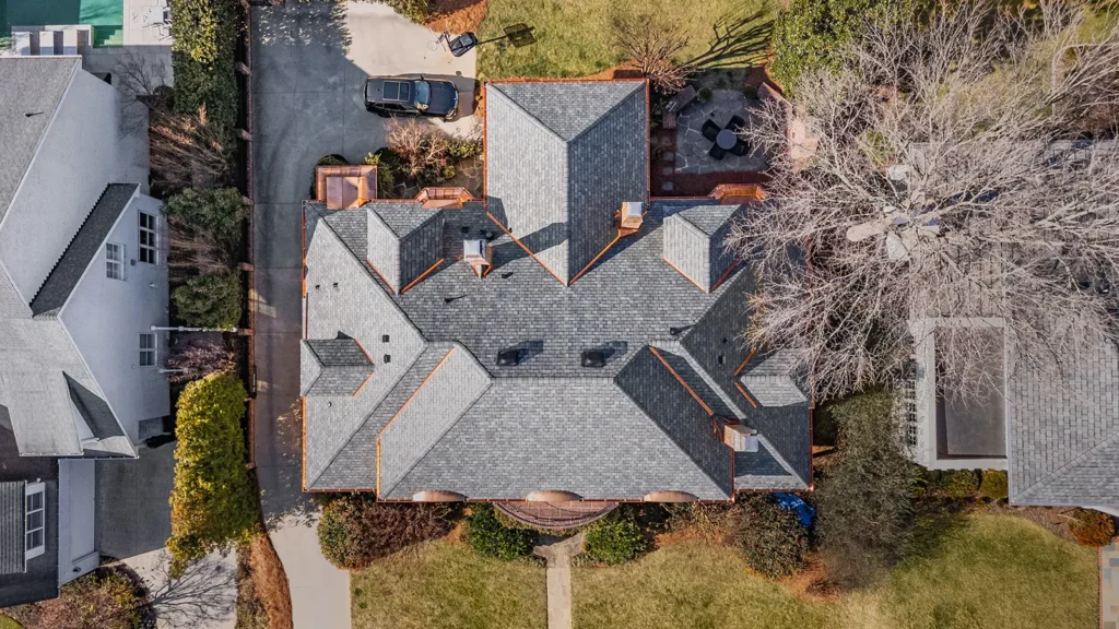 Aerial view of a residential house featuring a complex grey shingled roof with custom copper roofing, surrounded by a yard.