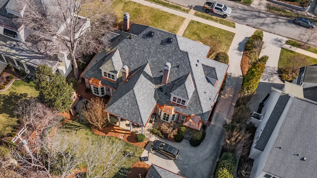 Aerial view of a large residential house in Greensboro, NC, featuring a complex gray shingled roof with copper roofing accents and a car parked in the driveway.