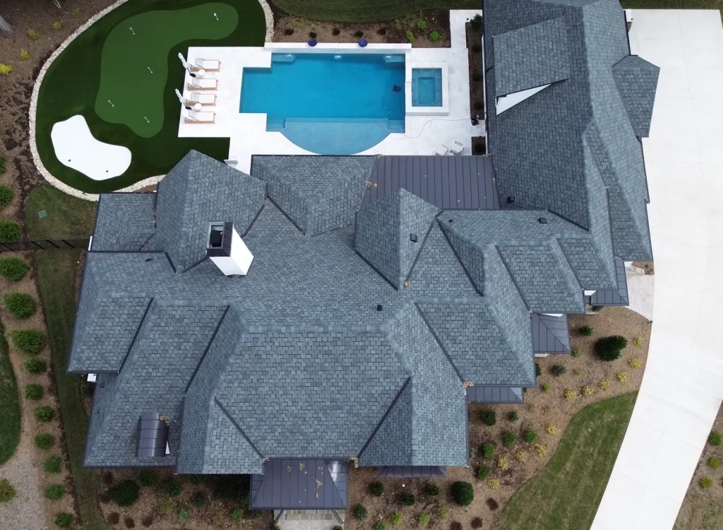 Aerial view of a house with a gray CertainTeed Belmont shingles roof, a backyard pool with lounge chairs, a hot tub, and a putting green surrounded by landscaped greenery.