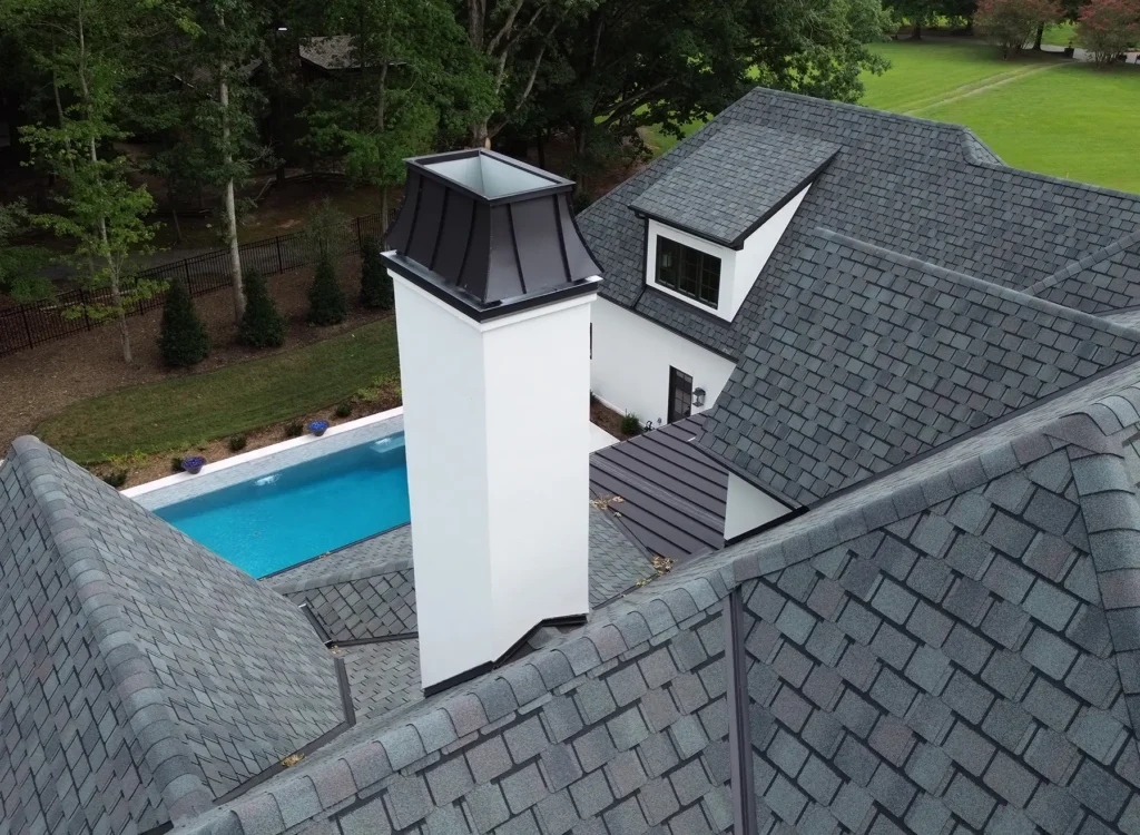 Aerial view of a house with CertainTeed Belmont shingles on a gray roof, white chimney, swimming pool, landscaped yard, and trees—showcasing quality Waxhaw NC roof installation.
