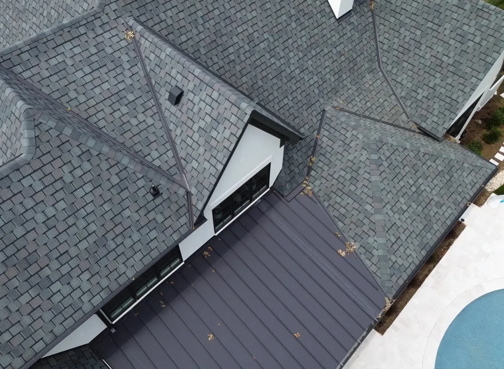 Aerial view of a house roof with CertainTeed Belmont shingles, white walls, a dark bronze metal roofing overhang, and a nearby round pool in Waxhaw NC. Some leaves are scattered on the roof.