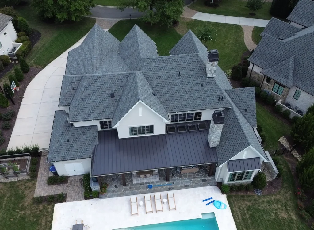 Aerial view of a large gray-roofed house with CertainTeed Belmont shingles, multiple gables, backyard patio, and swimming pool with lounge chairs. Lush green lawn surrounds this Waxhaw NC roof installation.