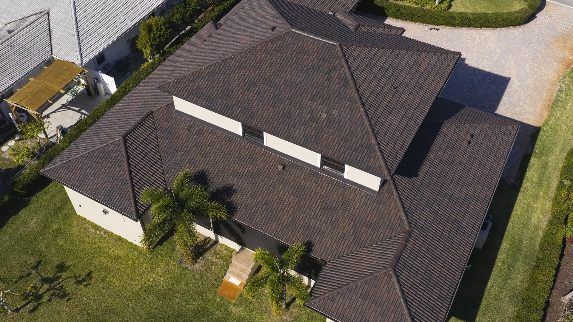 Aerial view of a house with a dark brown Brava composite roofing, two palm trees, and a surrounding lawn.