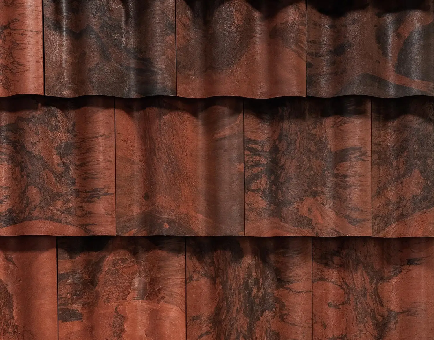 Overlapping rows of reddish-brown Brava composite roofing tiles featuring wavy designs and dark, marbled patterns.